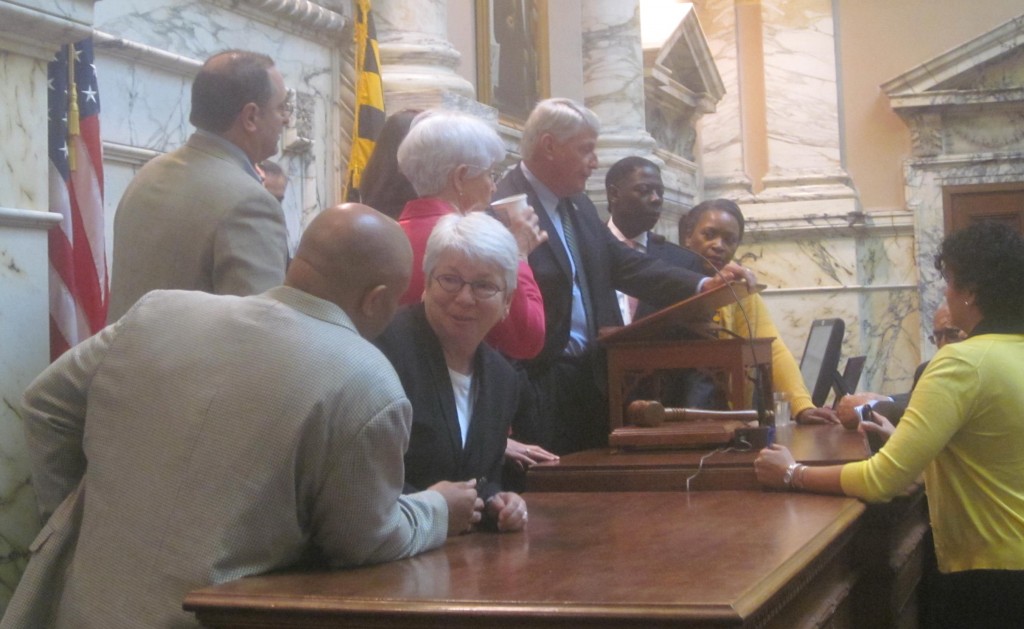 Assembly leaders confer with speaker at rostrum during special session.