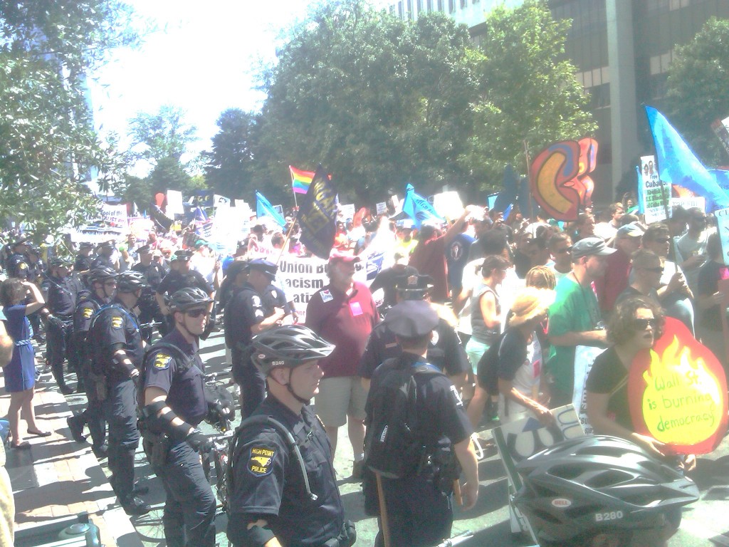 Police in bike helmets line street with parade of demonstrators.