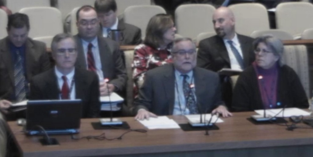 Warren Deschenaux, center at mic, surrounded by other fiscal analysts testifies on budget