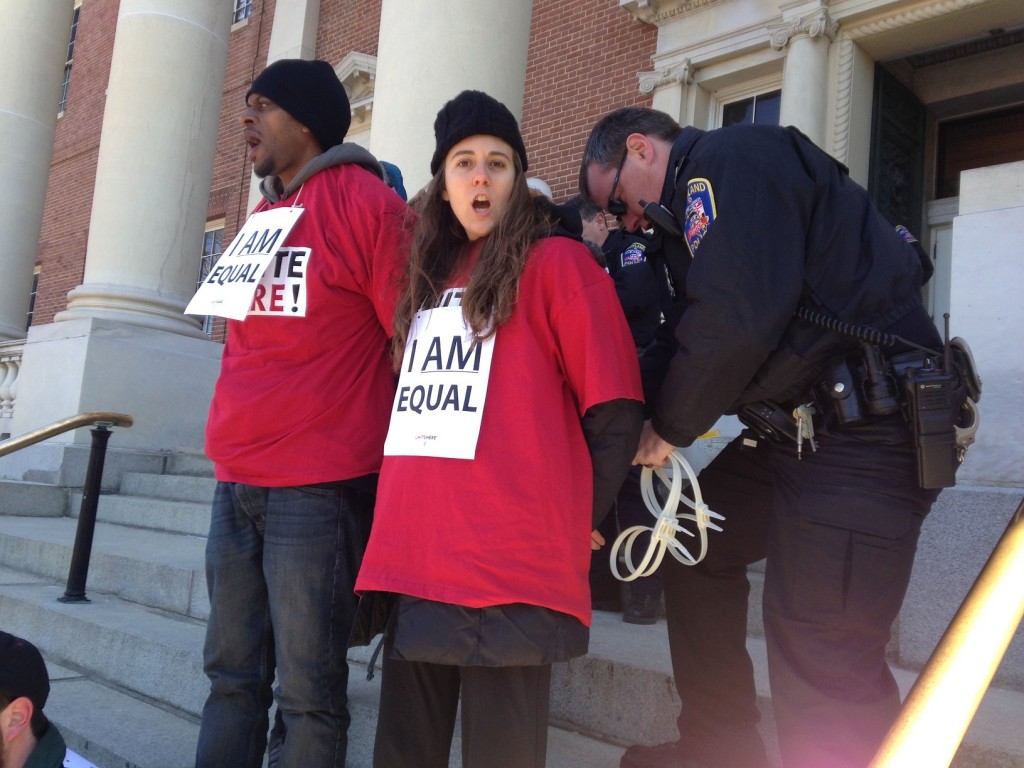 Fifteen Unite Here protesters stage sit-down on State House steps.