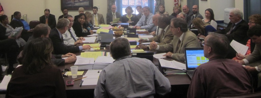 Delegates and staff on left meet with senators and staff on right to resolve budget differences with chief policy analyst Warren Deschenaux, center foreground, acting as moderator.